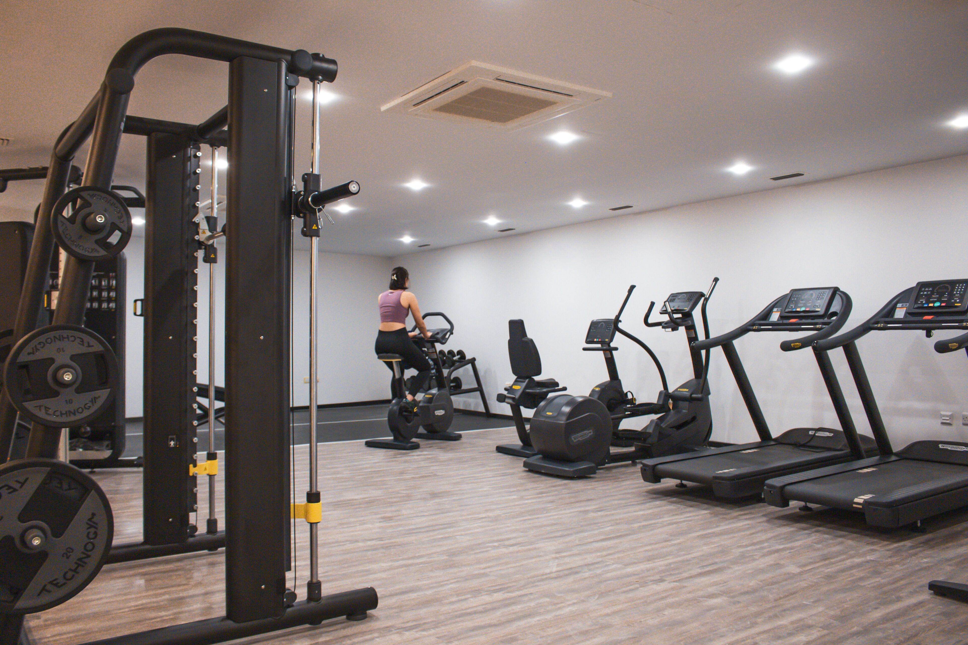 Une salle de sport équipée de machines de cardio, de matériel de musculation et où une personne s’entraîne.