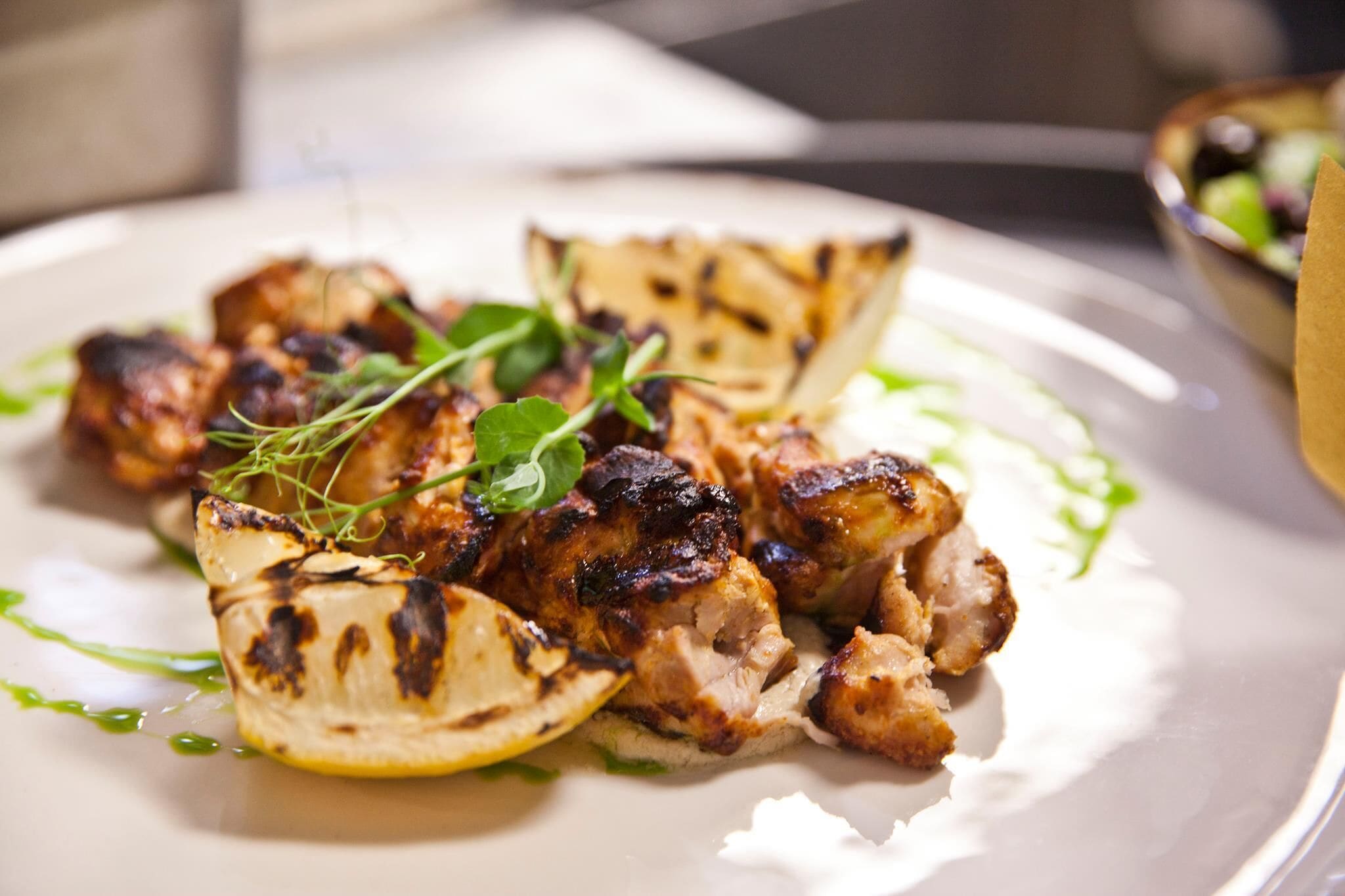 A plate with grilled chicken and lemon slices garnished with herbs.