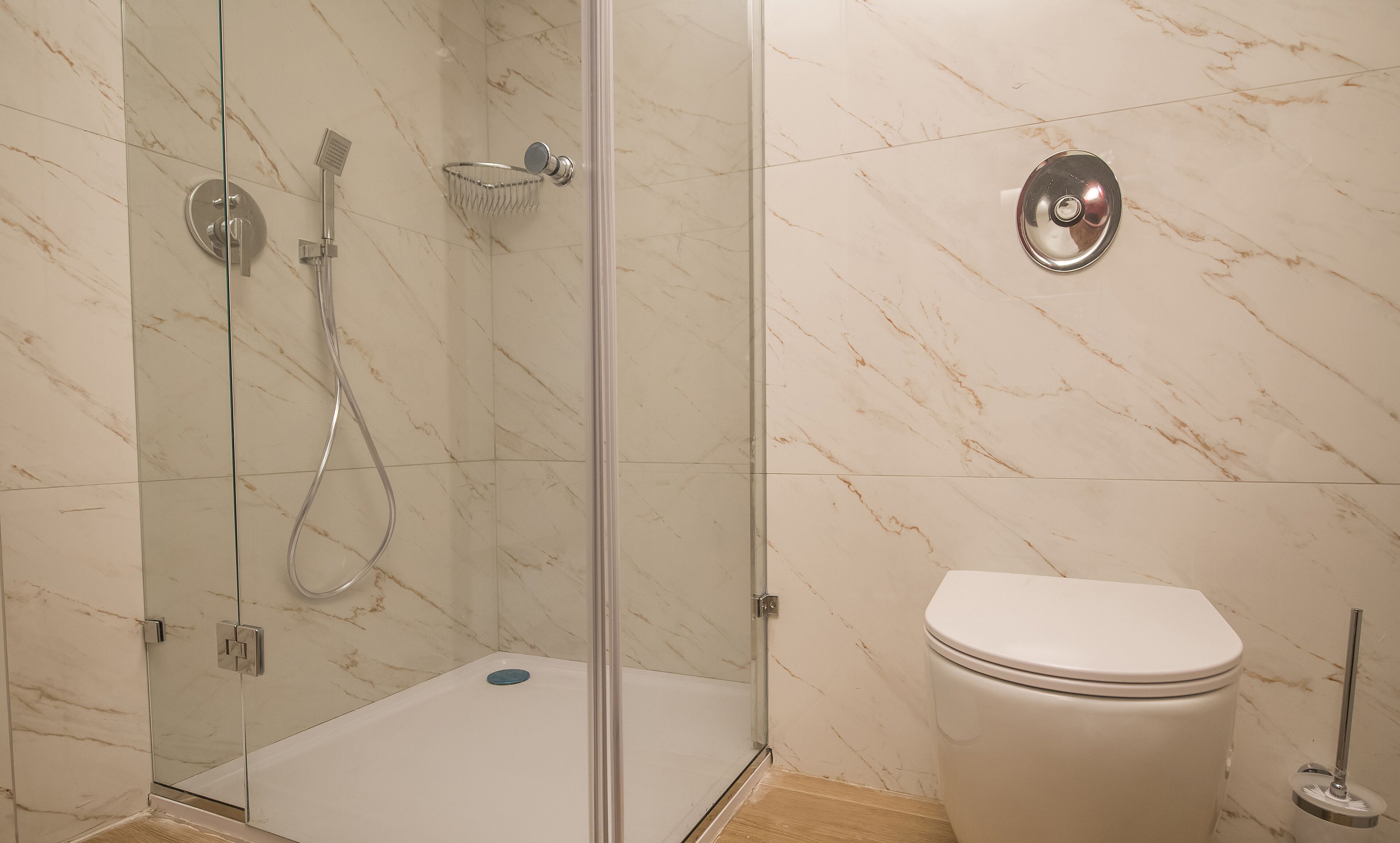 A bathroom with a glass-enclosed shower, a toilet, and a marble-patterned wall.
