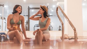 Two people sitting by a poolside in a well-lit indoor space with exercise equipment in the background. - Seaview Hotel Malta - Adults Only (St. Paul's Bay)