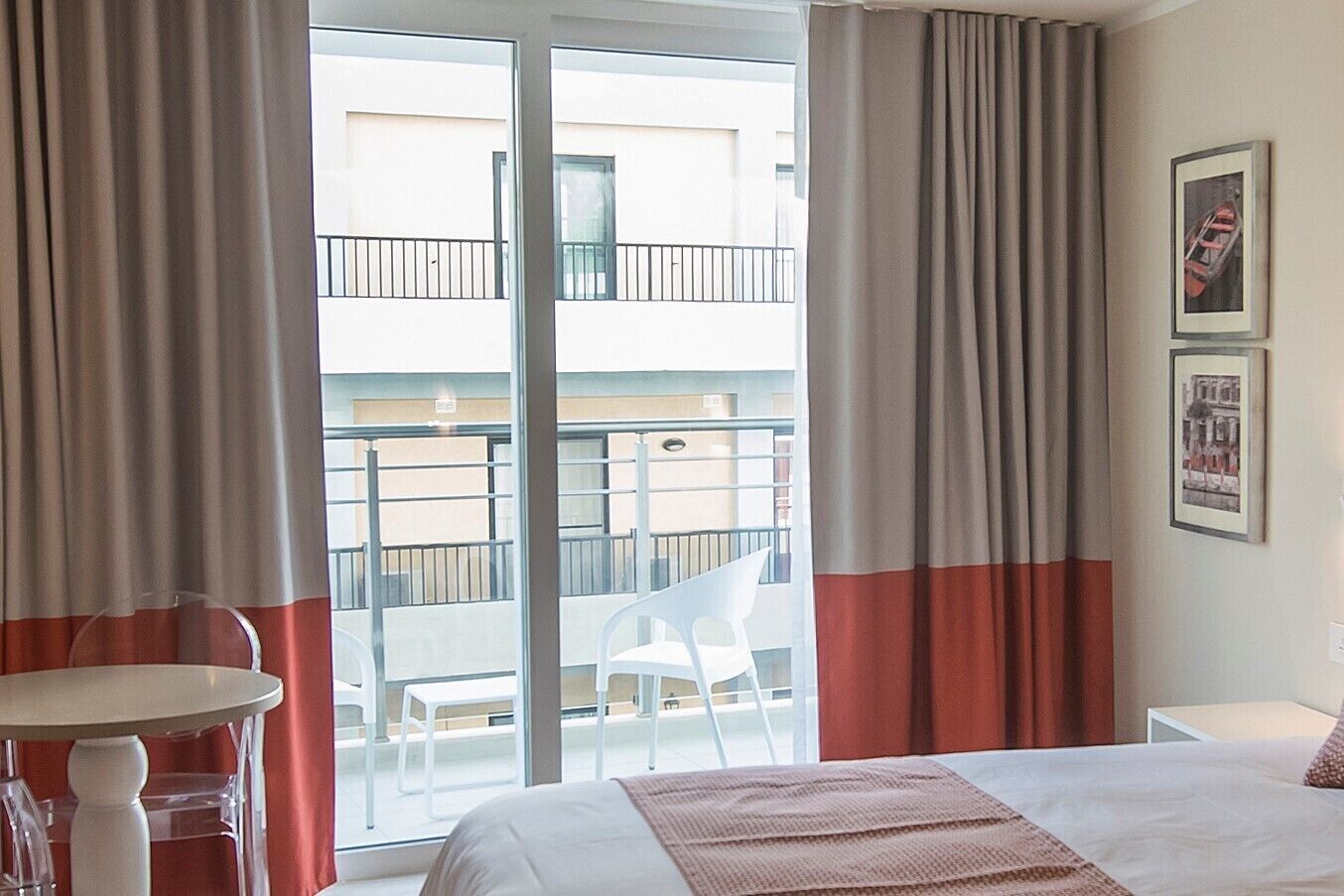 A hotel room with a bed, a small table, and chairs near a sliding glass door leading to a balcony.