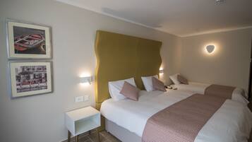Een hotelkamer met twee bedden, een witte nachtkastje en een wandplank.