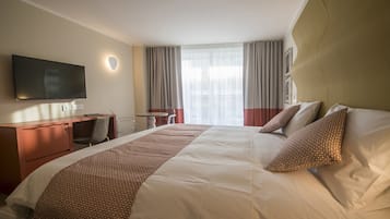 Habitación de hotel con cama, escritorio, silla, televisor y ventana con cortinas.