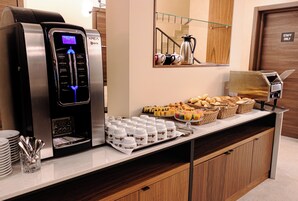 Una estación de café autoservicio con una máquina de café, tazas y una variedad de pasteles y panadería.