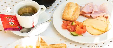 Un desayuno con tetera, taza, tostadas, huevos, frijoles, jamón, queso y tomates en platos.