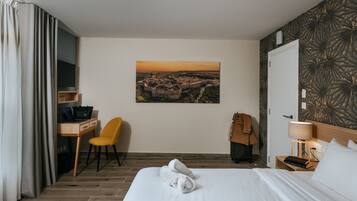 Habitación de hotel con cama, escritorio, silla, perchero y televisor montado en la pared.