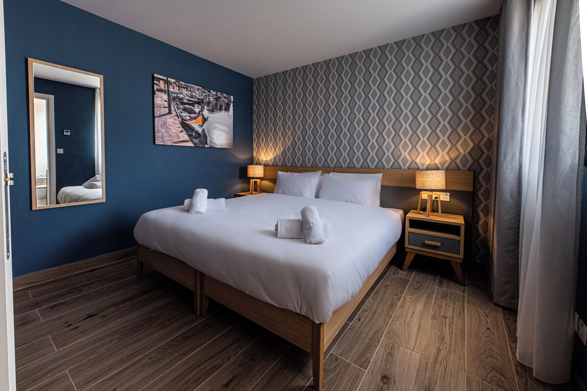 A hotel room with a large bed, two bedside tables, a mirror, a wall-mounted picture, and a patterned wall.