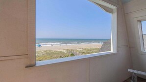 Une pièce dotée d’une grande fenêtre donnant sur une plage, d’un plancher en bois et d’un mur blanc.