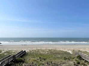 Une plage avec une promenade en bois qui mène au rivage, une plage de sable et l’océan.