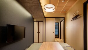 Habitació tradicional japonesa amb tatami, una taula de fusta baixa, portes corredisses i un televisor penjat.