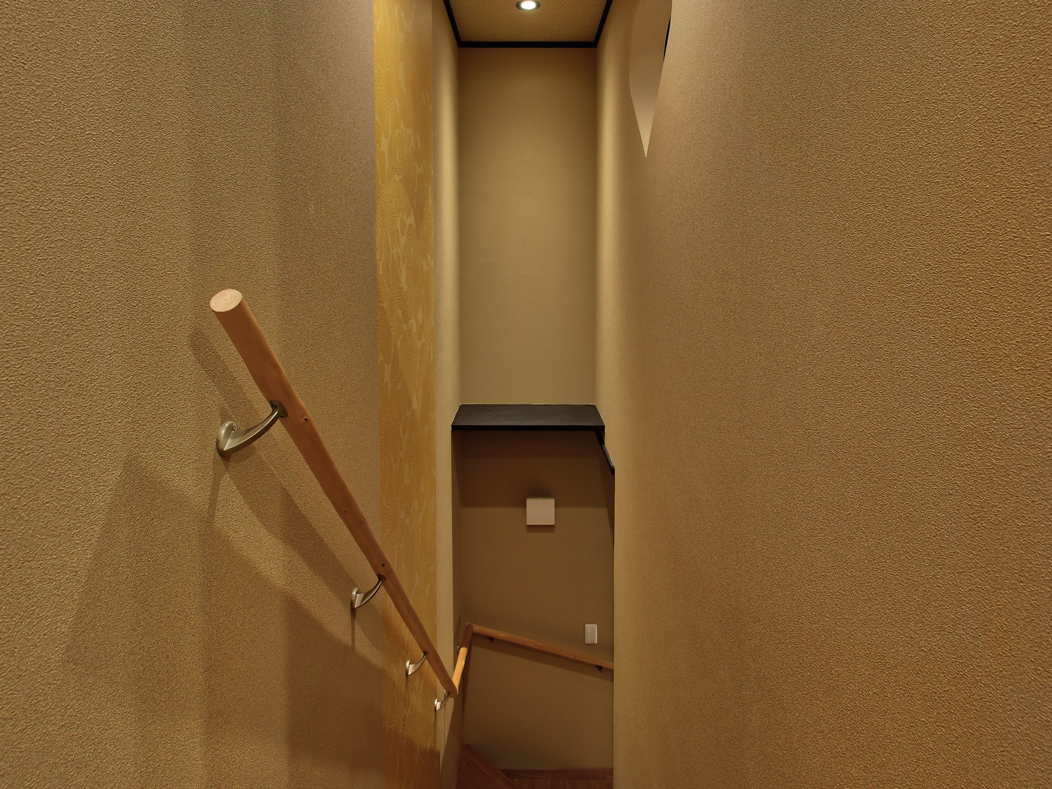 A narrow hallway with a wooden handrail and a textured wall.