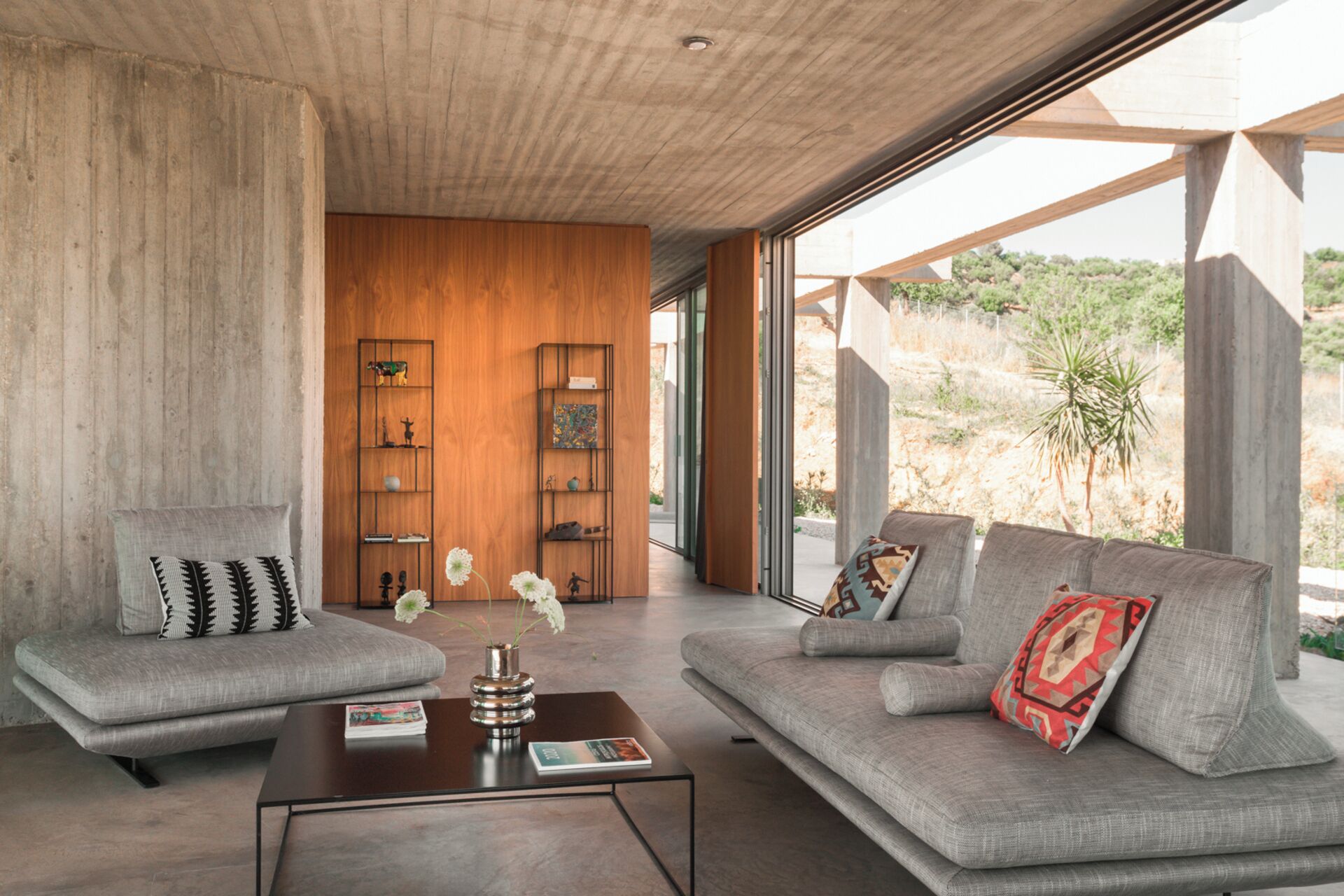 A modern living room with two grey sofas, a coffee table, and wooden shelving with decorative items.