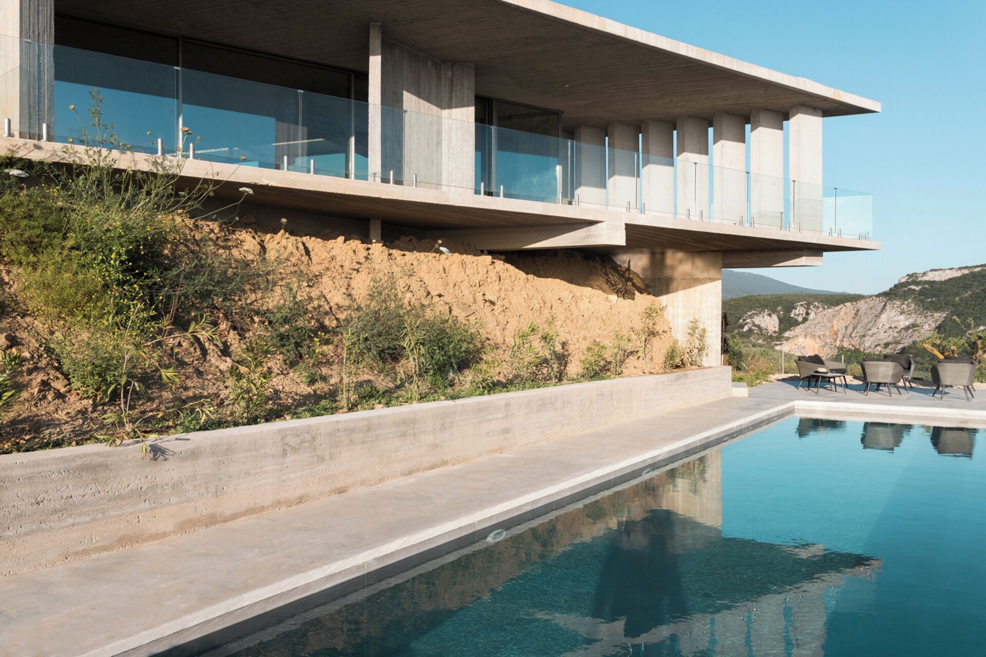 Un edifici modern amb piscina, pilars de formigó i vistes al paisatge.