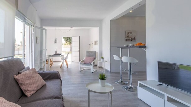 A modern living room with a sofa, TV, and a dining area in the background. - Villa El Almendro by Costa CarpeDiem (Calpe)
