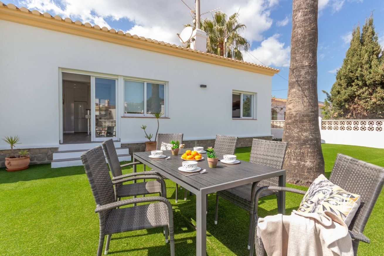A patio with a table set for dining, surrounded by wicker chairs, and a palm tree in the background.
