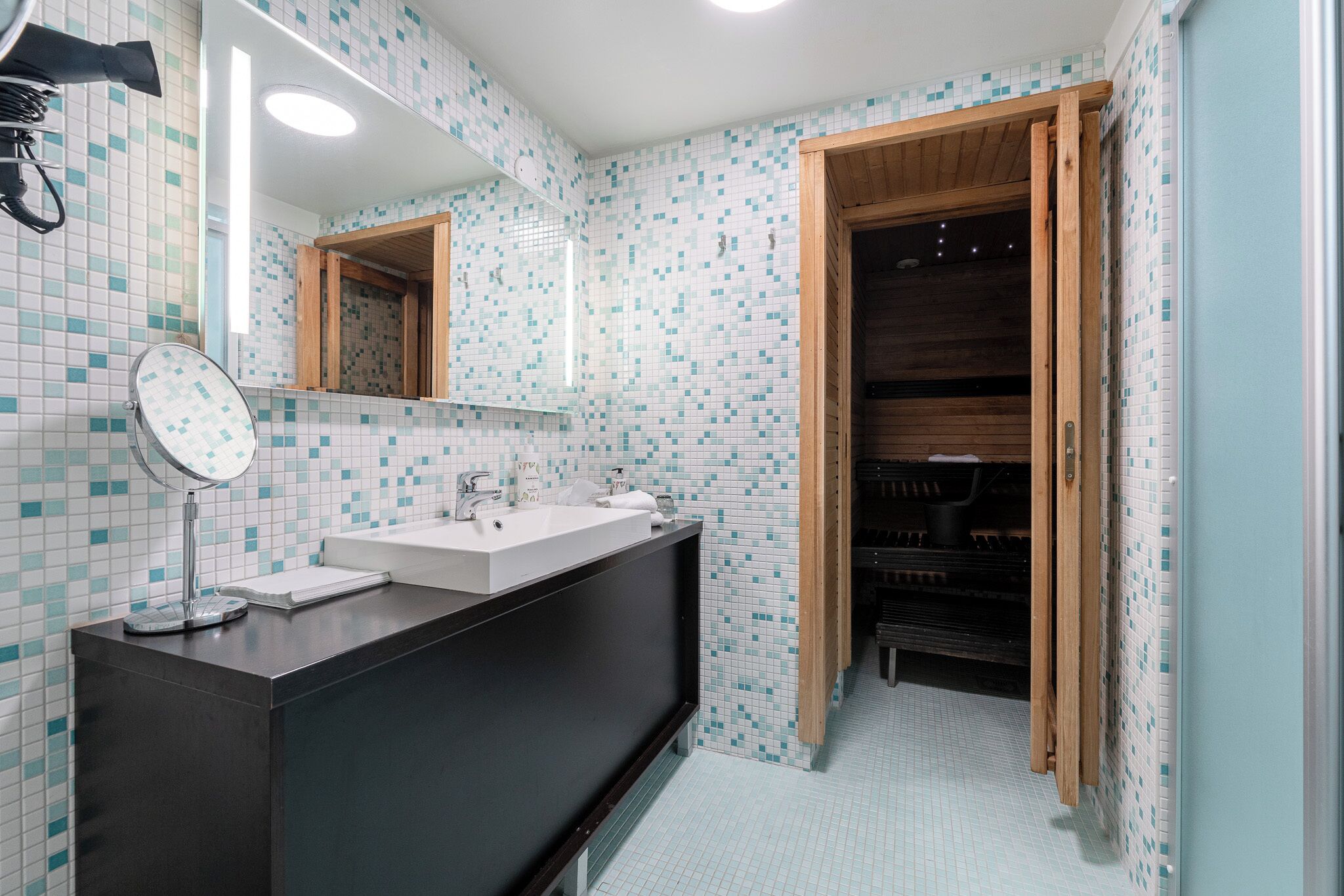 Un baño moderno con lavamanos doble, un espejo y una puerta de madera que da a la zona de la ducha.