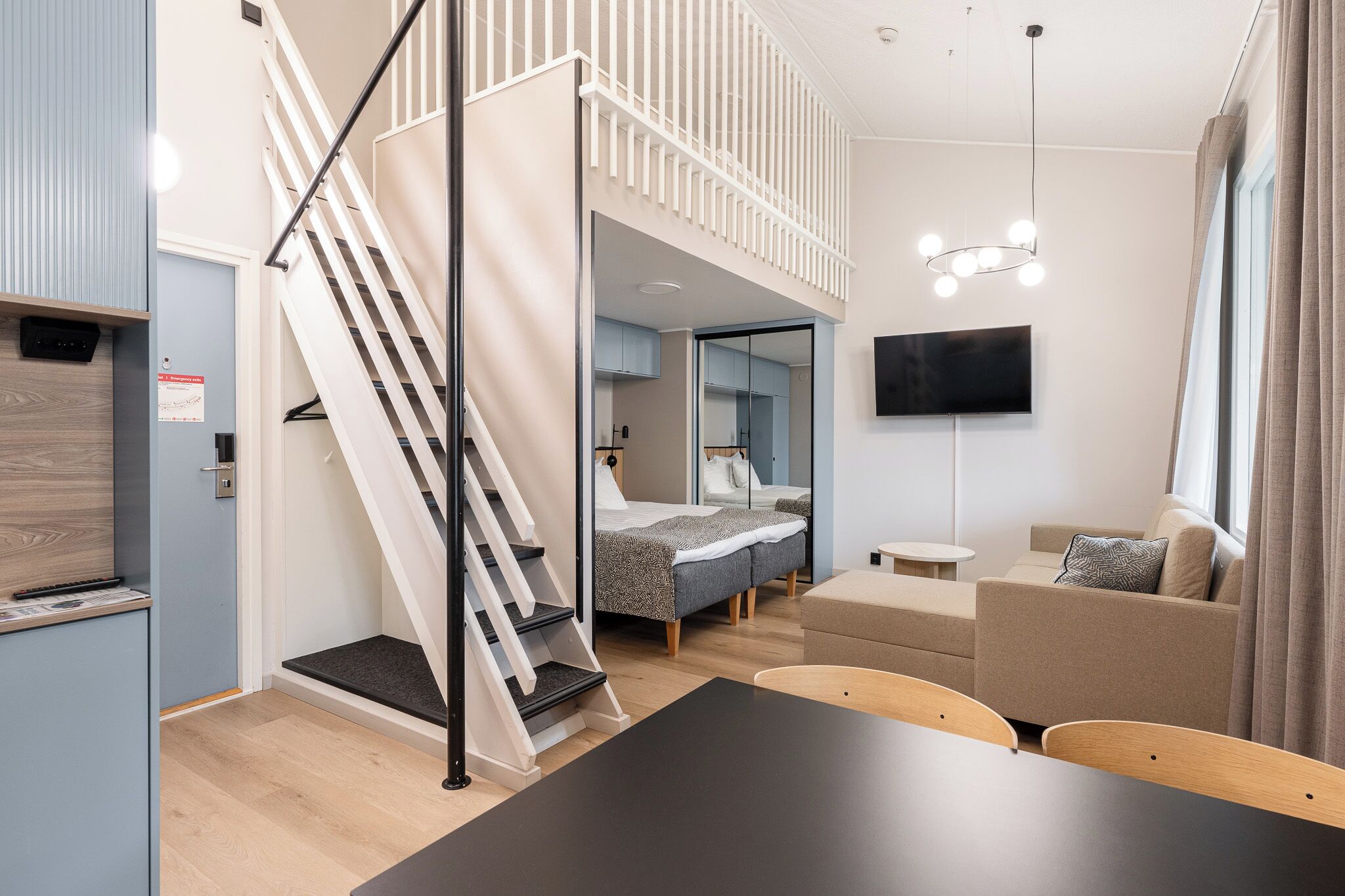 Moderni hotellihuone, jossa on parveltaan varustettu sänky, sohva, ruokapöytä ja televisio.