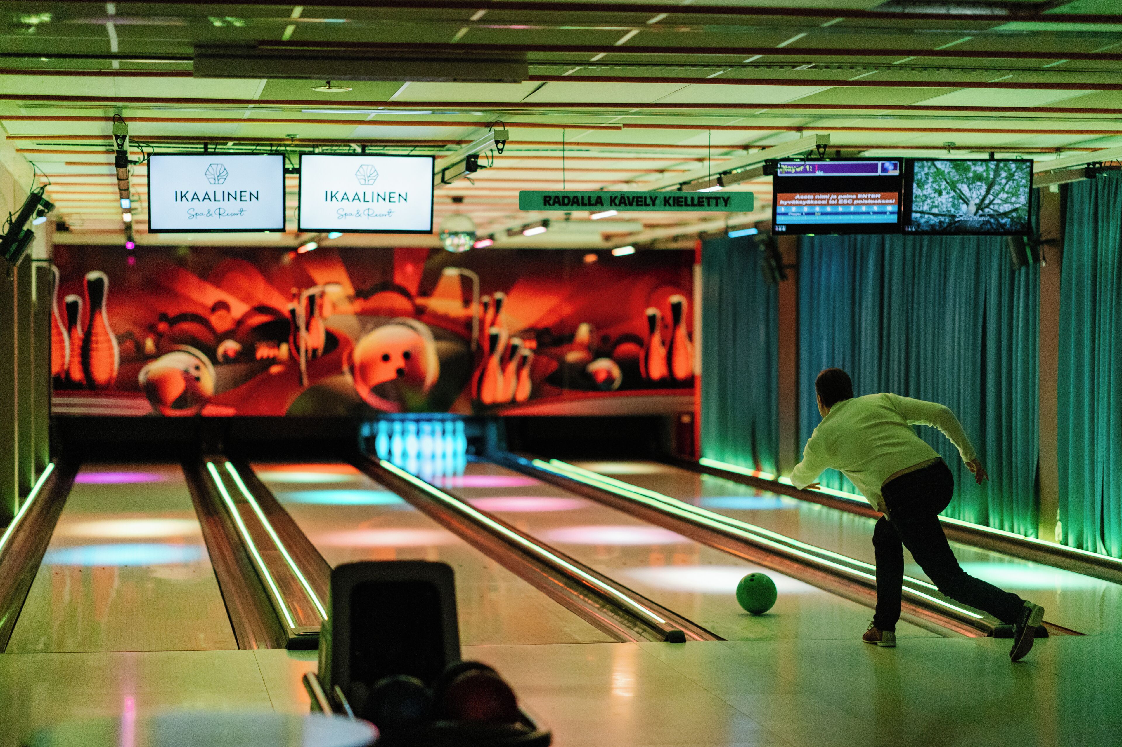 Une salle de bowling avec des pistes, une boule de bowling en mouvement et une personne qui joue au bowling.