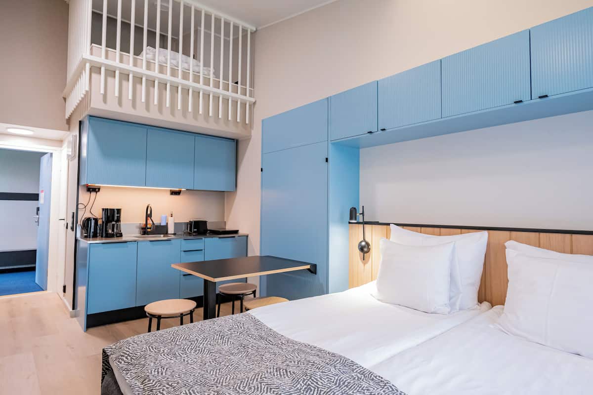 Hotellihuone, jossa on kerrossänky, työpöytä tuolilla, pieni keittotila ja sänky valkoisilla vuodevaatteilla.