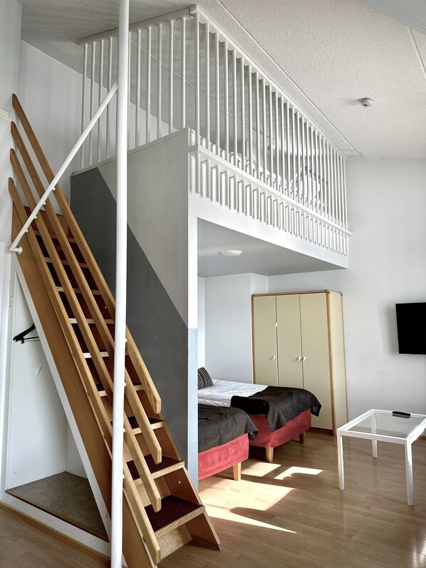 Dormitorio tipo loft con escalera de madera, cama, armario y televisor en la pared.