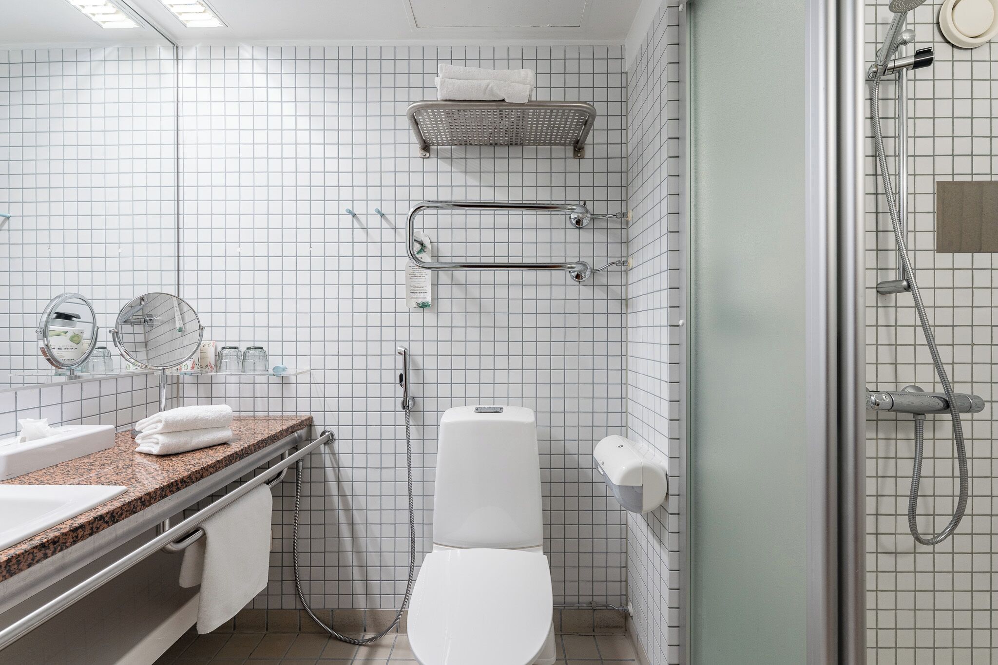 A modern bathroom with a white toilet, a sink with a granite countertop, a mirror, and a shower area.