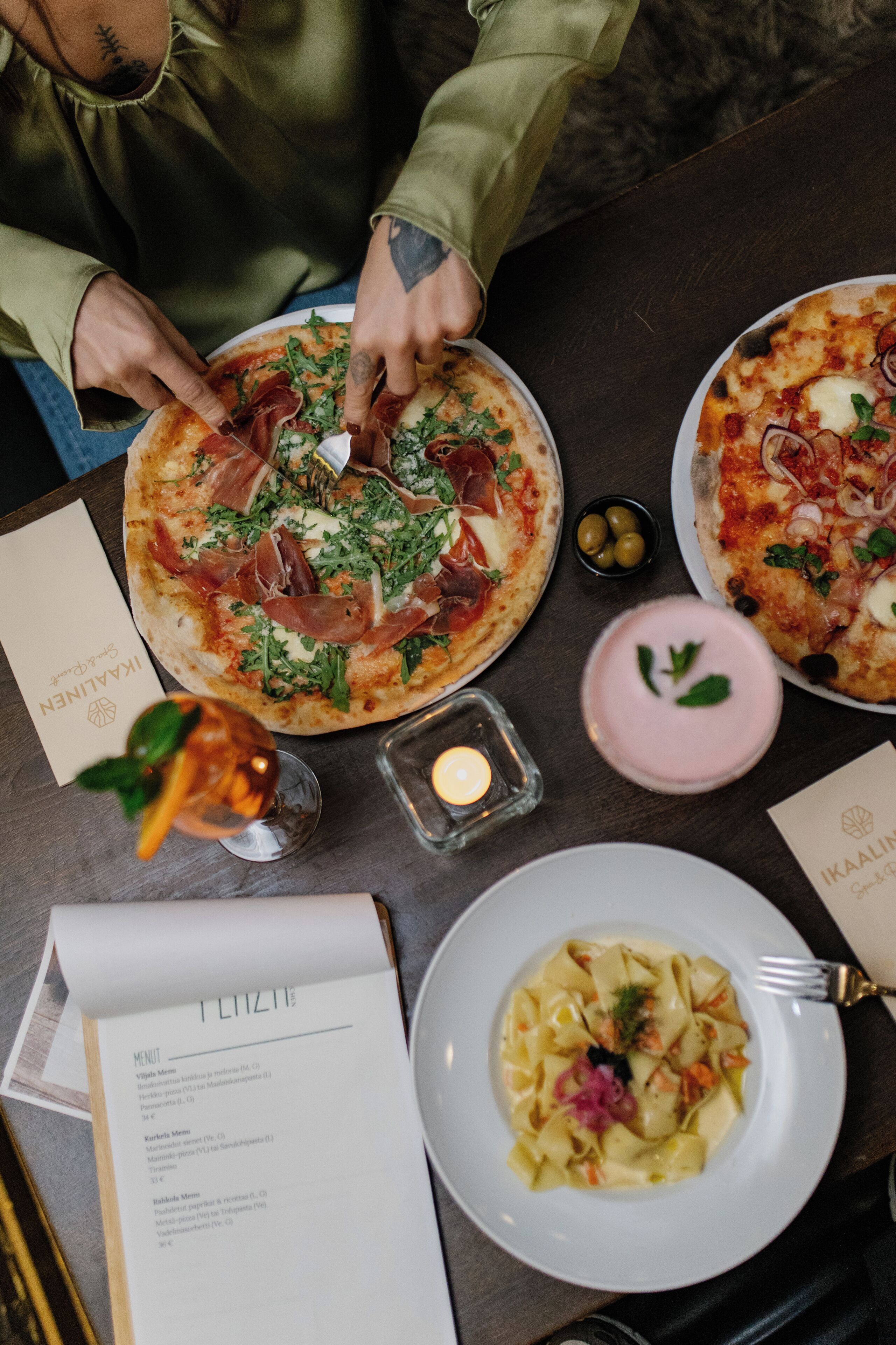 A dining table with a pizza, a plate of pasta, a menu, and a candle.
