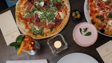 A dining table with a pizza, a plate of pasta, a menu, and a candle.