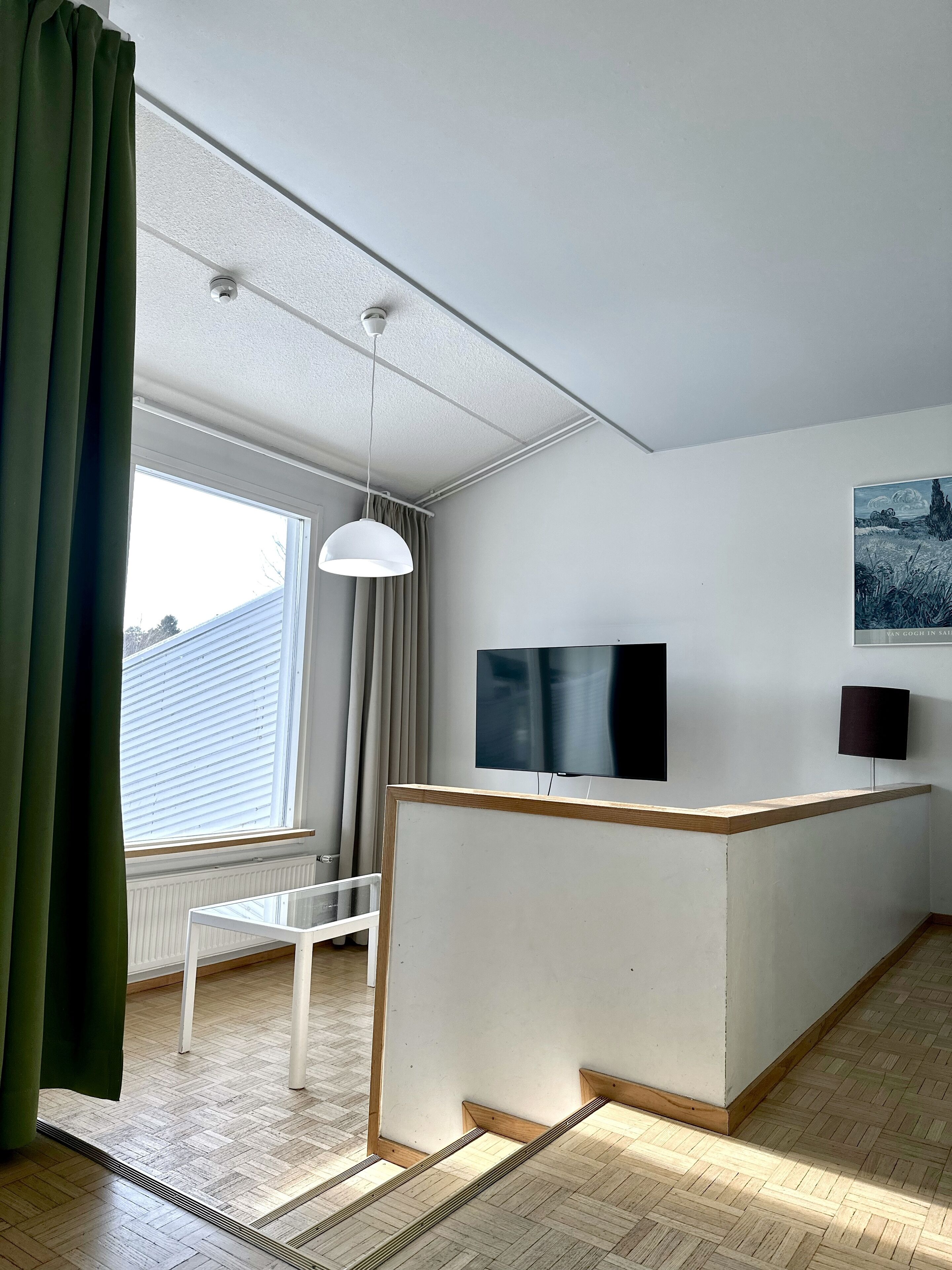 Una sala de estar moderna con techo blanco, un ventanal con cortinas, una mesa blanca y un mostrador de recepción de madera.
