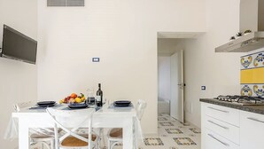 Una cucina compatta con un tavolo da pranzo per due persone, pensili bianchi, un fornello a gas e piastrelle del pavimento decorate.