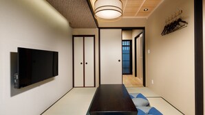 Una habitación de estilo japonés tradicional con suelo de tatami, una mesita baja y un televisor montado en la pared.