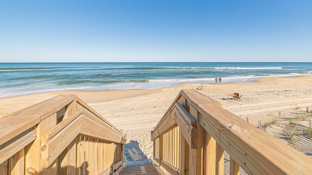 Een houten looppad dat naar een zandstrand leidt, met de oceaan op de achtergrond.