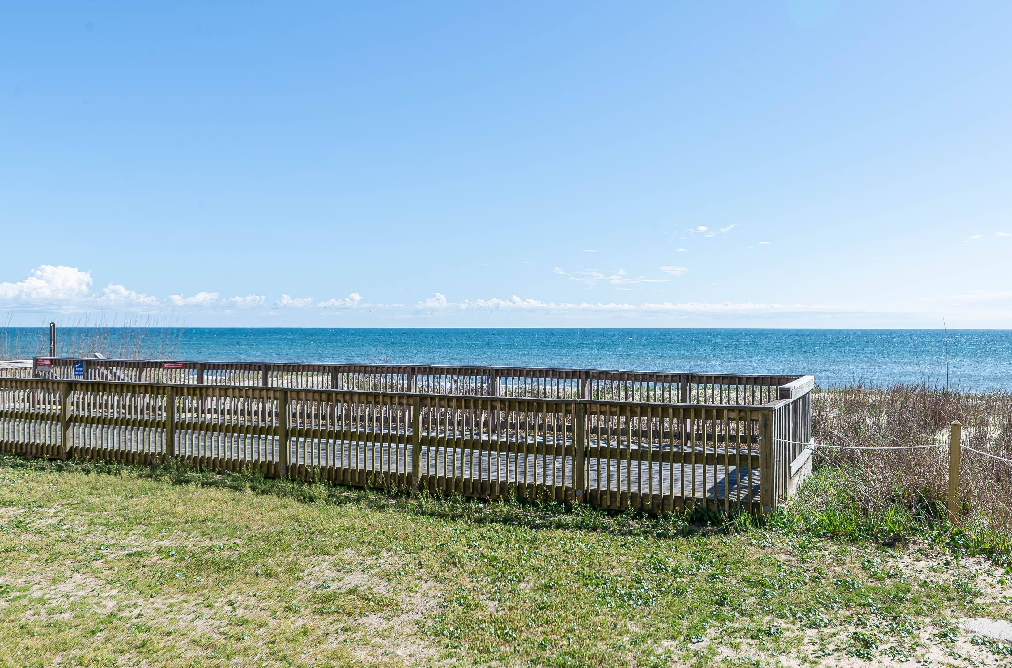 A wooden fence overlooking a beach with a clear view of the ocean.