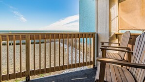 Een houten terras met uitzicht op het strand, buitenmeubels en een gebouw met een blauwe gevel.