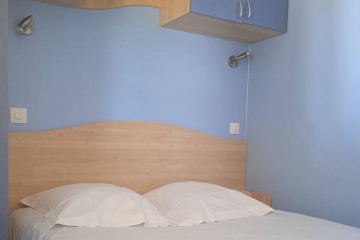 Ein Schlafzimmer mit Holz-Kopfteil, einem Bett mit weißer Bettwäsche und Einbauschränken über dem Bett.