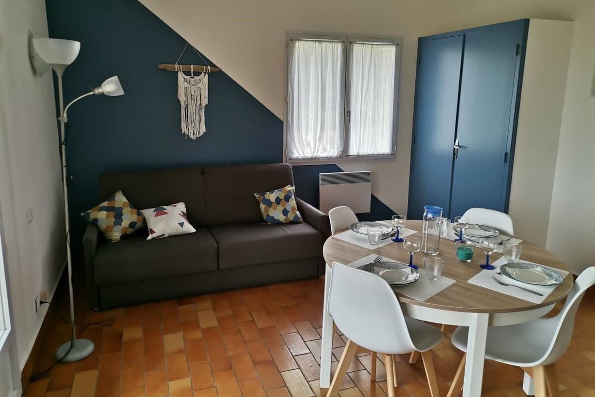 Ein gemütliches Wohnzimmer mit einem dunklen Sofa, einem Esstisch für zwei Personen und einem großen blauen Kleiderschrank.