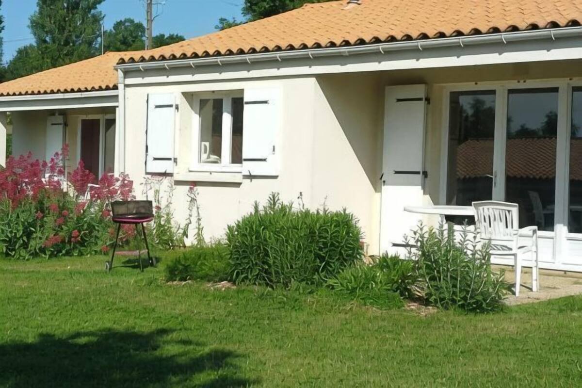 Ein weißes Gebäude mit Ziegeldach, einer Terrasse mit Tisch und Stühlen sowie einem kleinen Garten mit rosa Blumen.