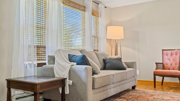 A living room with a grey sofa, a small wooden side table, a floor lamp, and a patterned rug.