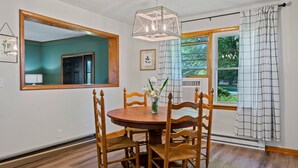 A dining area with a wooden table and chairs, a large mirror, and a window with curtains.