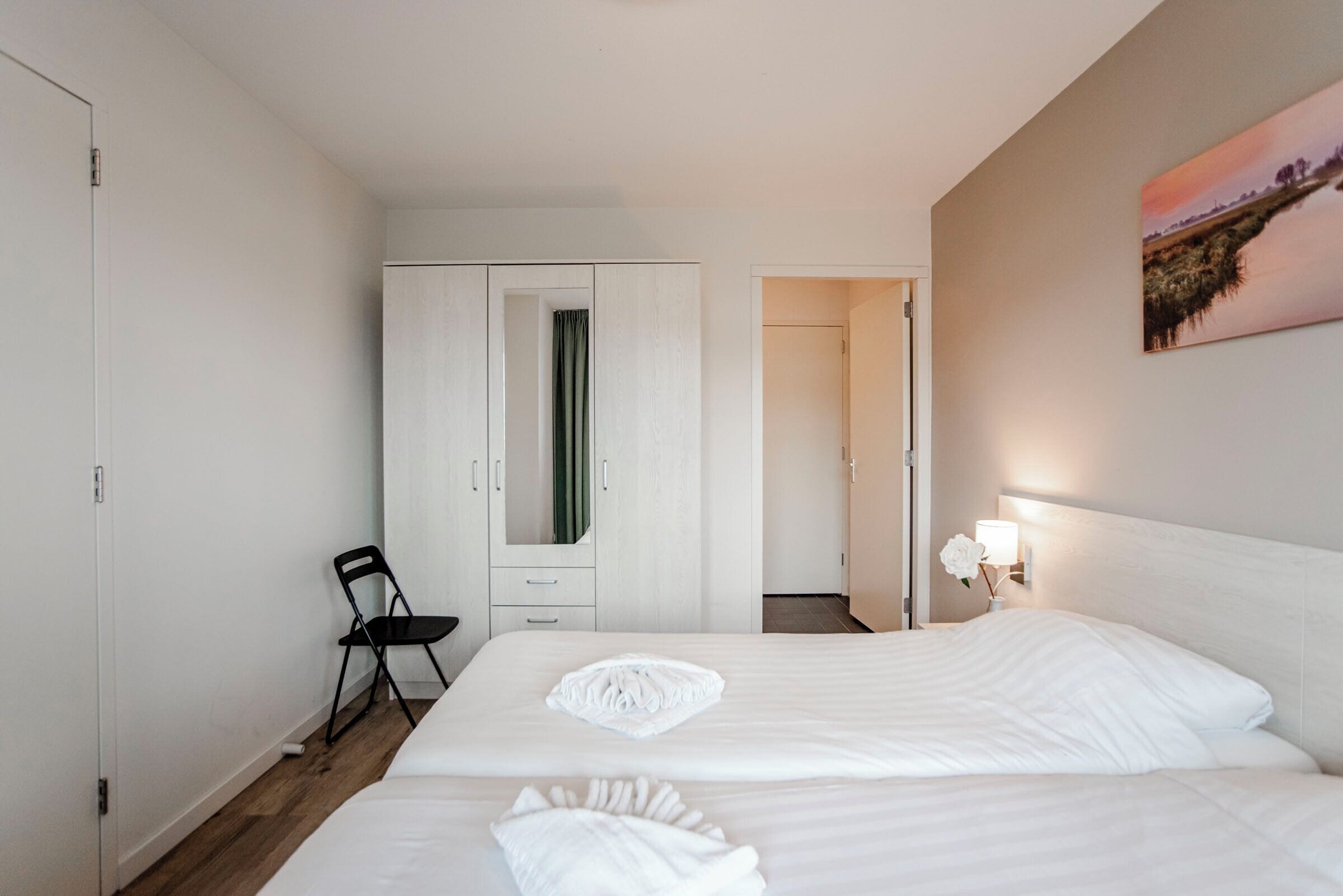 Une chambre d’hôtel avec deux lits, une armoire, une chaise et un tableau au mur.