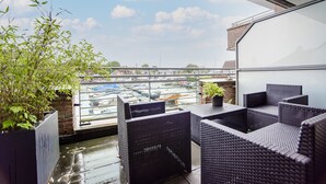 A balcony with wicker furniture and a potted plant, overlooking a marina with boats.