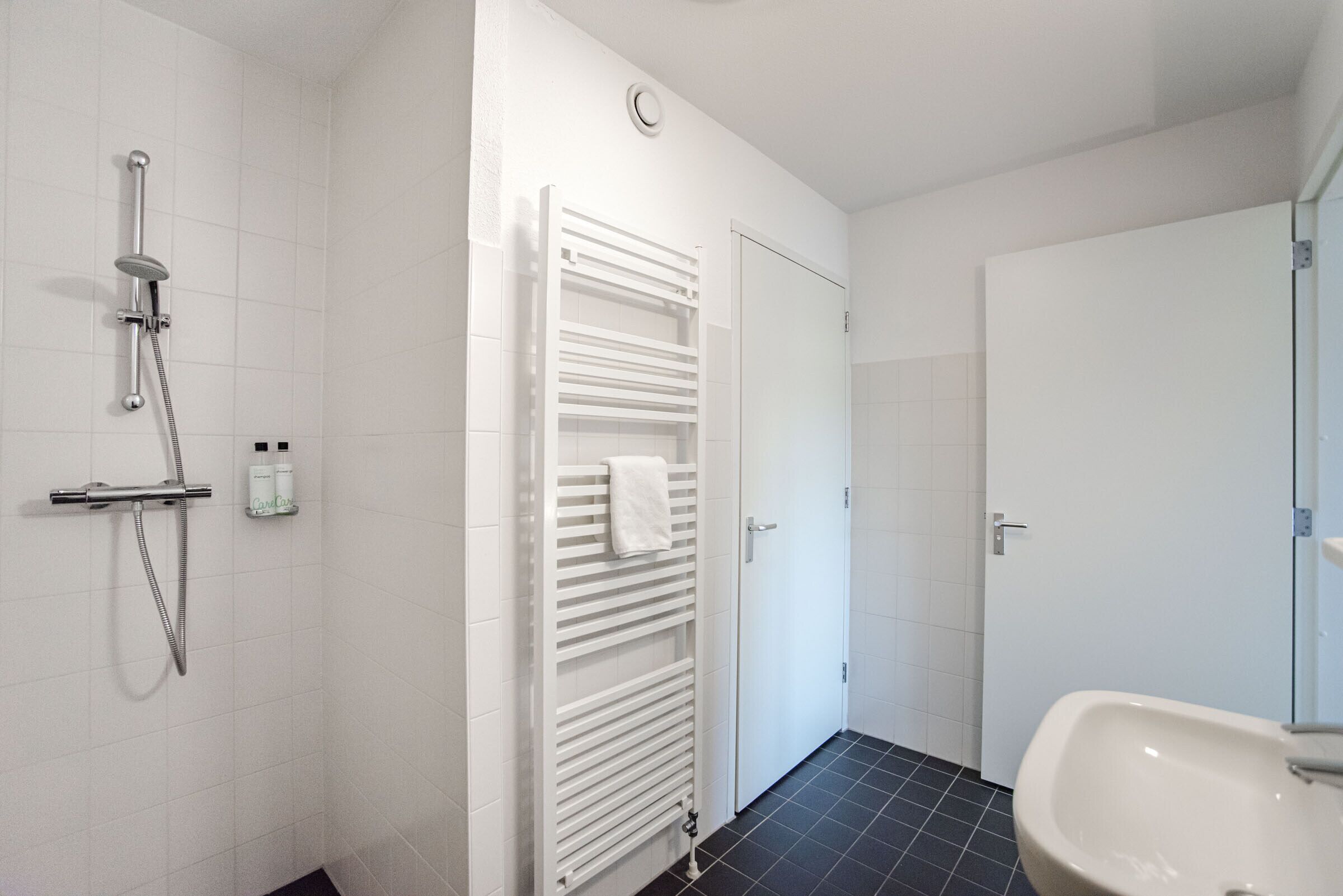 A modern bathroom with a shower, a towel rack, a sink, and a toilet.