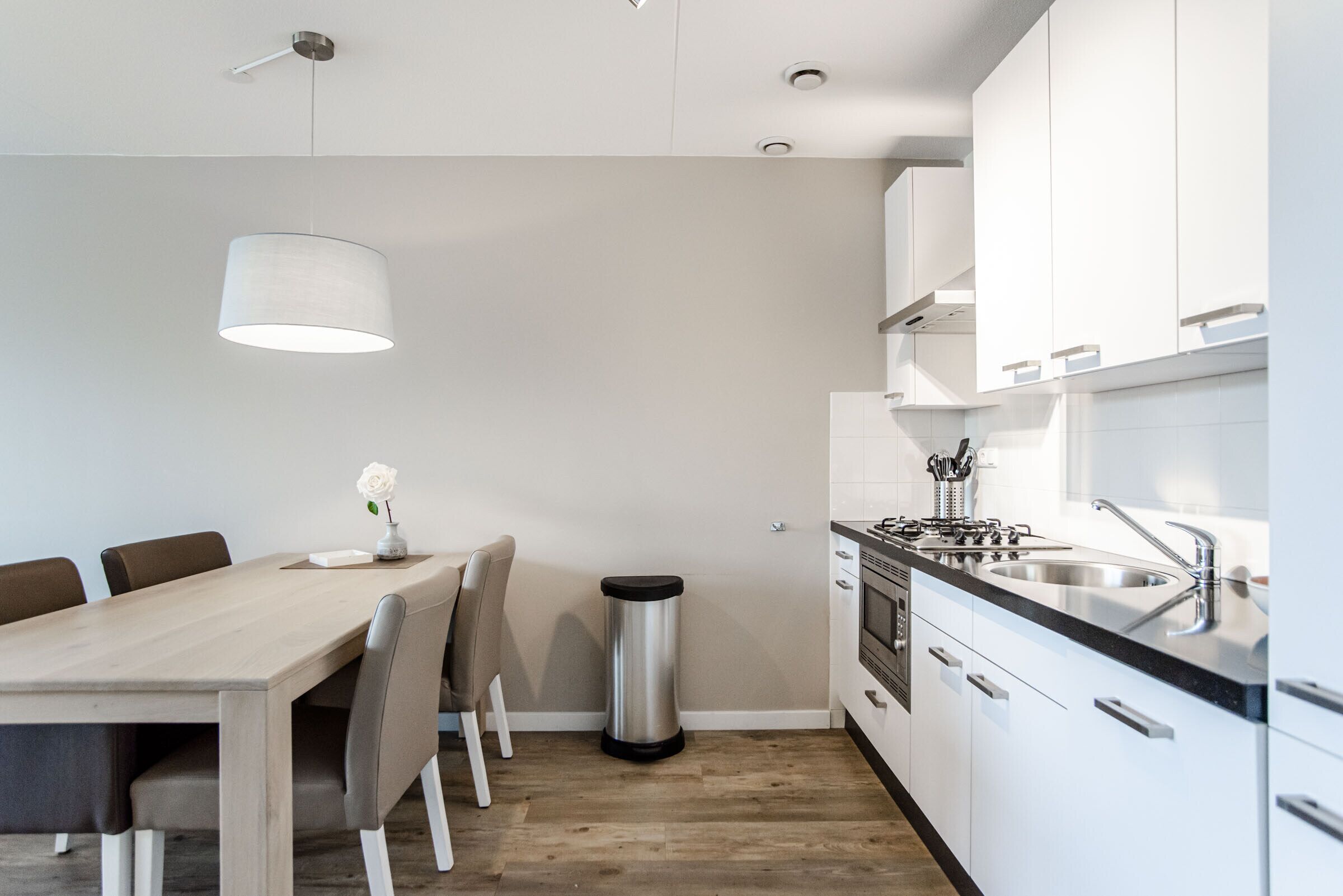 Une cuisine moderne avec des meubles blancs, un évier en acier inoxydable et une table à manger en bois.