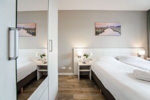 Quarto de hotel com duas camas, piso de madeira e duas mesas de cabeceira com luminárias e flores.