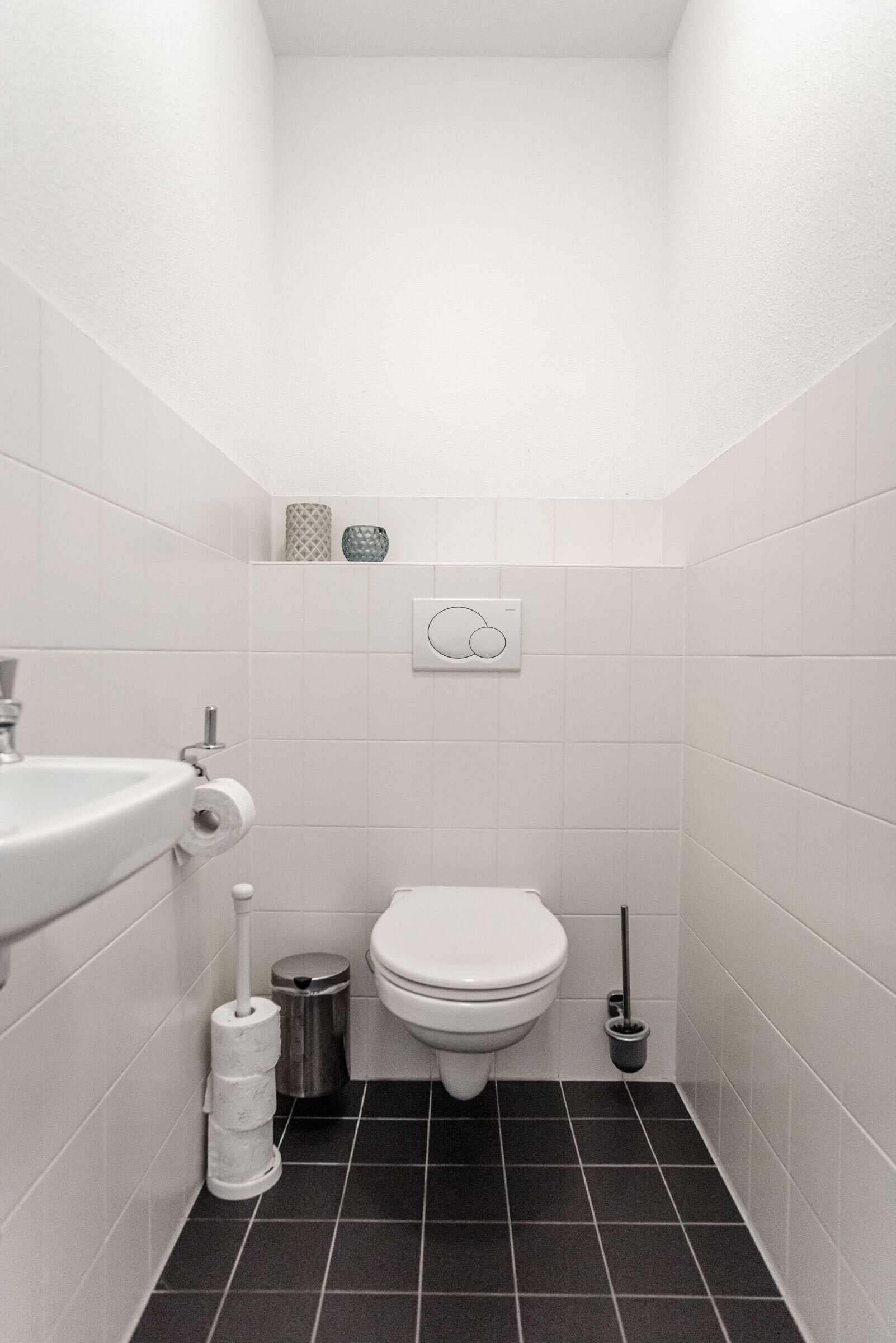 A small, white-walled bathroom with a white toilet, a sink, and a toilet paper holder.
