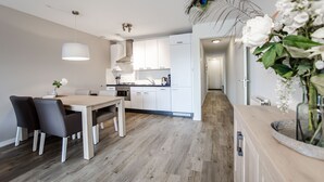 A modern kitchen with white cabinets, a wooden dining table, and chairs. There is a peacock feather decoration on the ceiling and a vase with flowers on the counter.