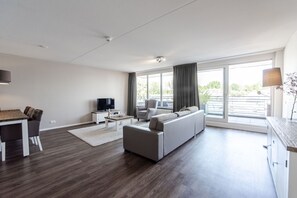 Relax in a spacious living room with a large window offering a view of the outdoors, a comfortable sofa, and a dining area with a table and chairs.