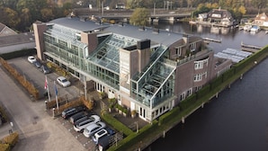 A modern hotel with a glass facade, a parking lot, and a river view. - Spacious and luxurious apartment - Kaag Resort (15) (Warmond)