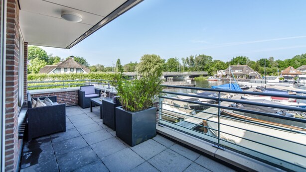 A balcony with outdoor seating, a potted plant, and a view of boats and houses across the water. - Spacious and luxurious apartment - Kaag Resort (15) (Warmond)