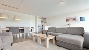 A modern living room with a grey sofa, a wooden coffee table, and a dining area with a white table and chairs. - Spacious and luxurious apartment - Kaag Resort (26) (Warmond)
