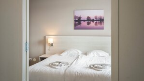 A hotel room with a bed, a nightstand, a wall-mounted lamp, and a painting of a landscape. - Spacious and luxurious apartment - Kaag Resort (26) (Warmond)